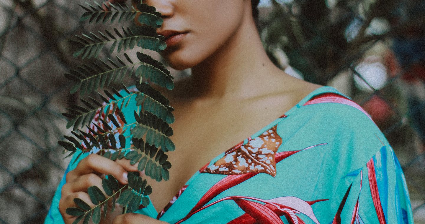 A girl posed with a plant in her hand, she is in a bright blue shirt with flower patterns